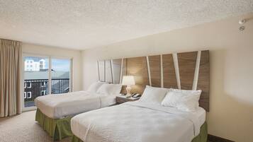 A hotel room with two beds, a balcony with a view, and a modern headboard.