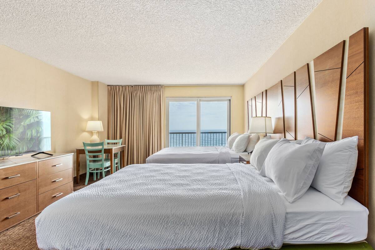 Een hotelkamer met twee bedden, een bureau met stoel, een televisie en uitzicht op de oceaan.