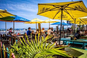 Terras met gele parasols, uitzicht op het strand en mensen aan het dineren.