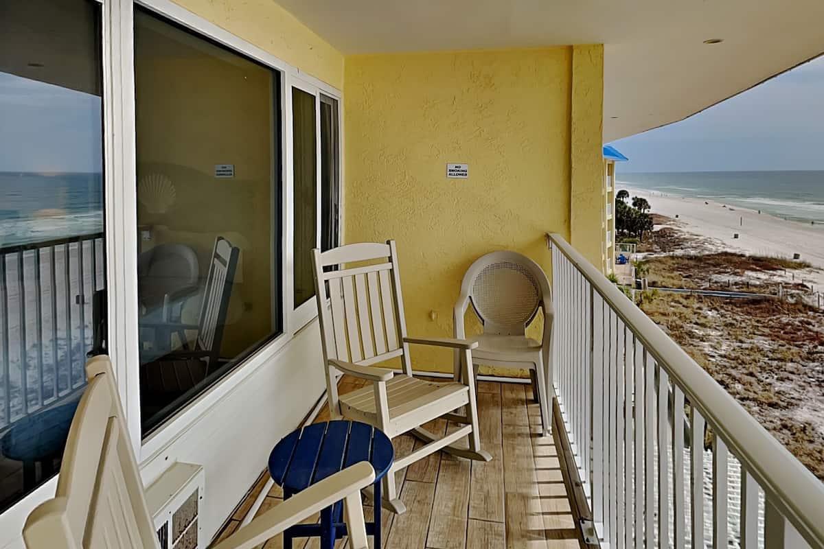 A balcony with a view of the beach, a chair, and a table.