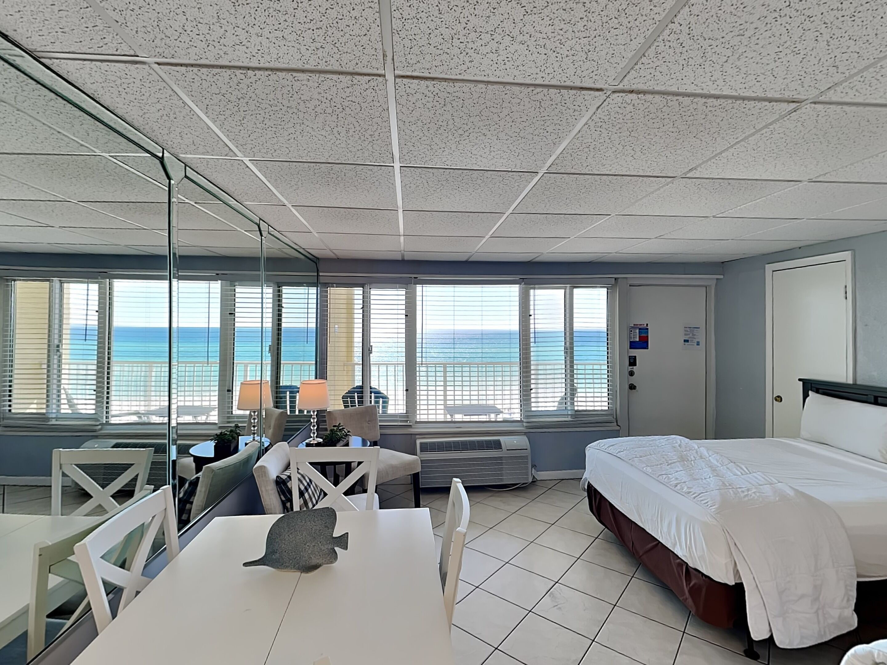 A hotel room with a bed, a desk, a chair, a table, and a large window with a view of the ocean.