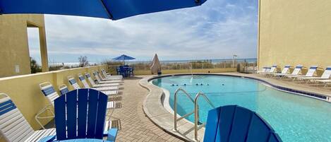 Ein Poolbereich mit blauen Liegestühlen und Sonnenschirmen, einem Pool und Blick auf den Strand.