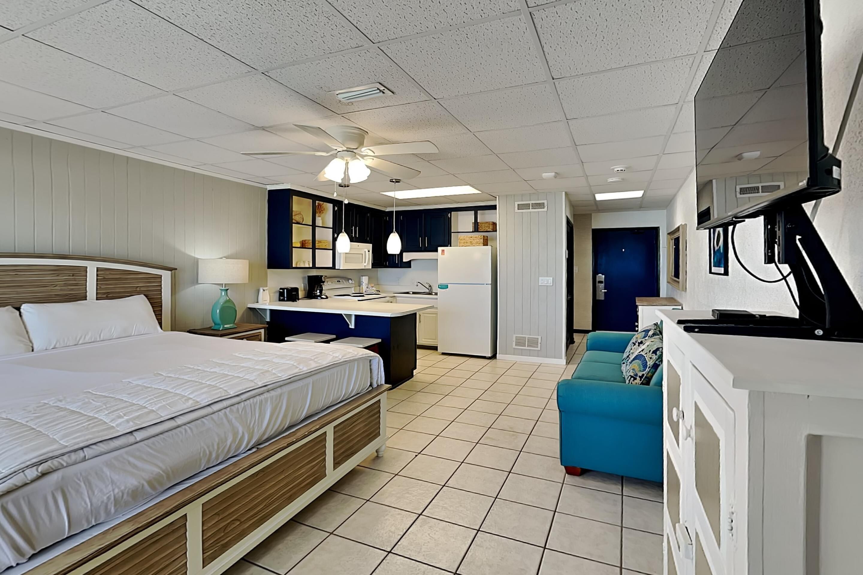 A compact hotel room with a bed, kitchenette, and a small seating area.