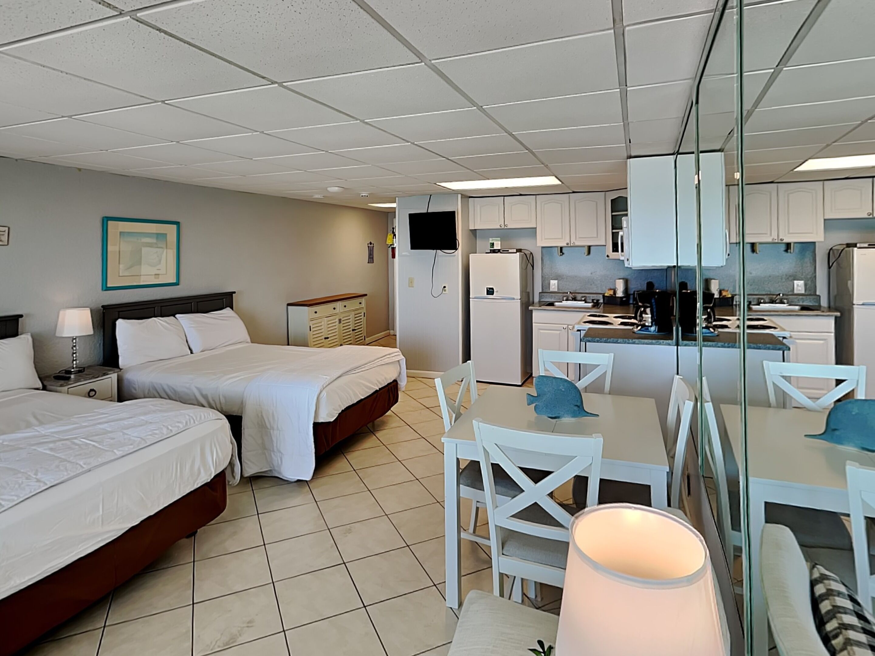Una habitación de hotel con dos camas, una kitchenette y un comedor con sillas y una mesa.