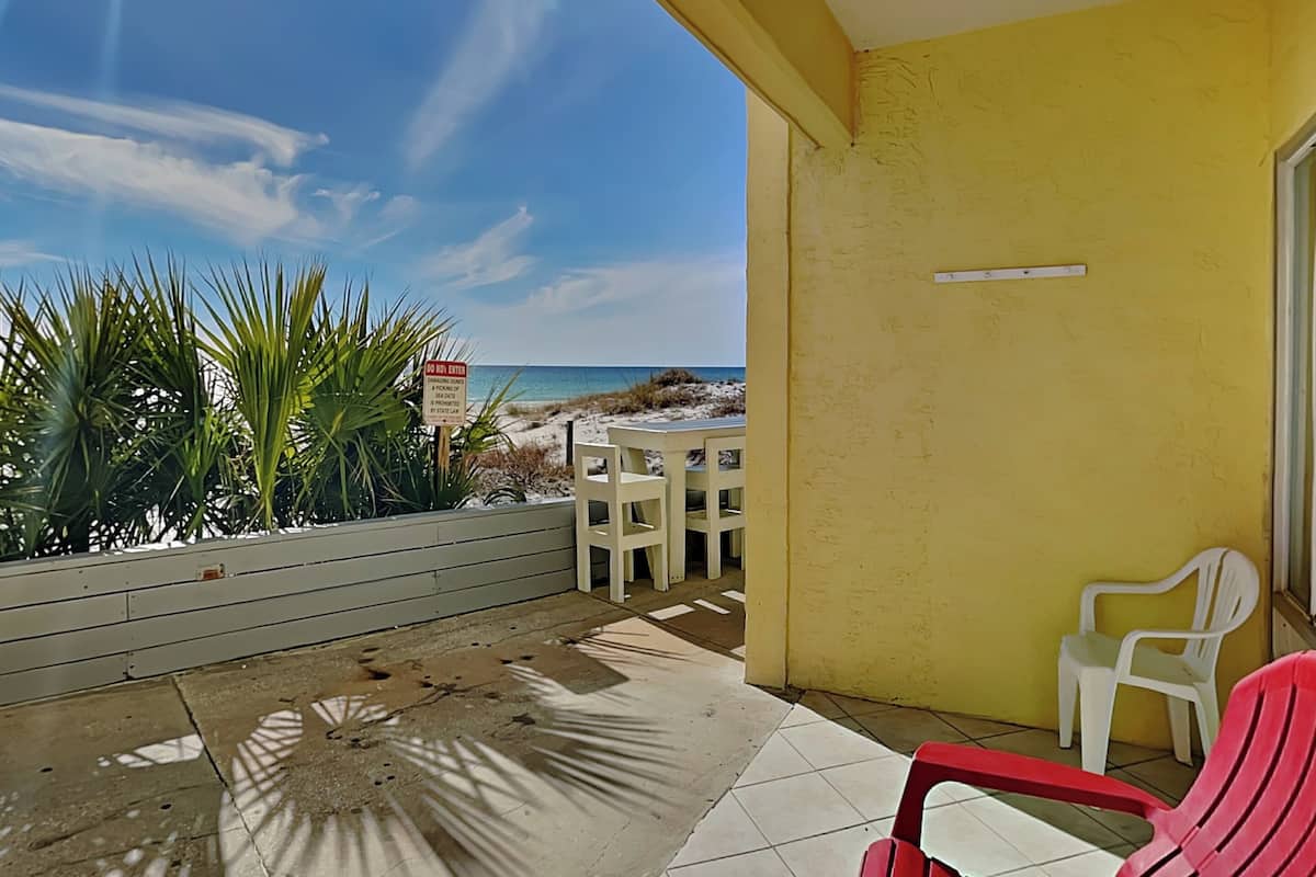 A balcony with a view of the beach, a 'DO NOT ENTER' sign, and two chairs.