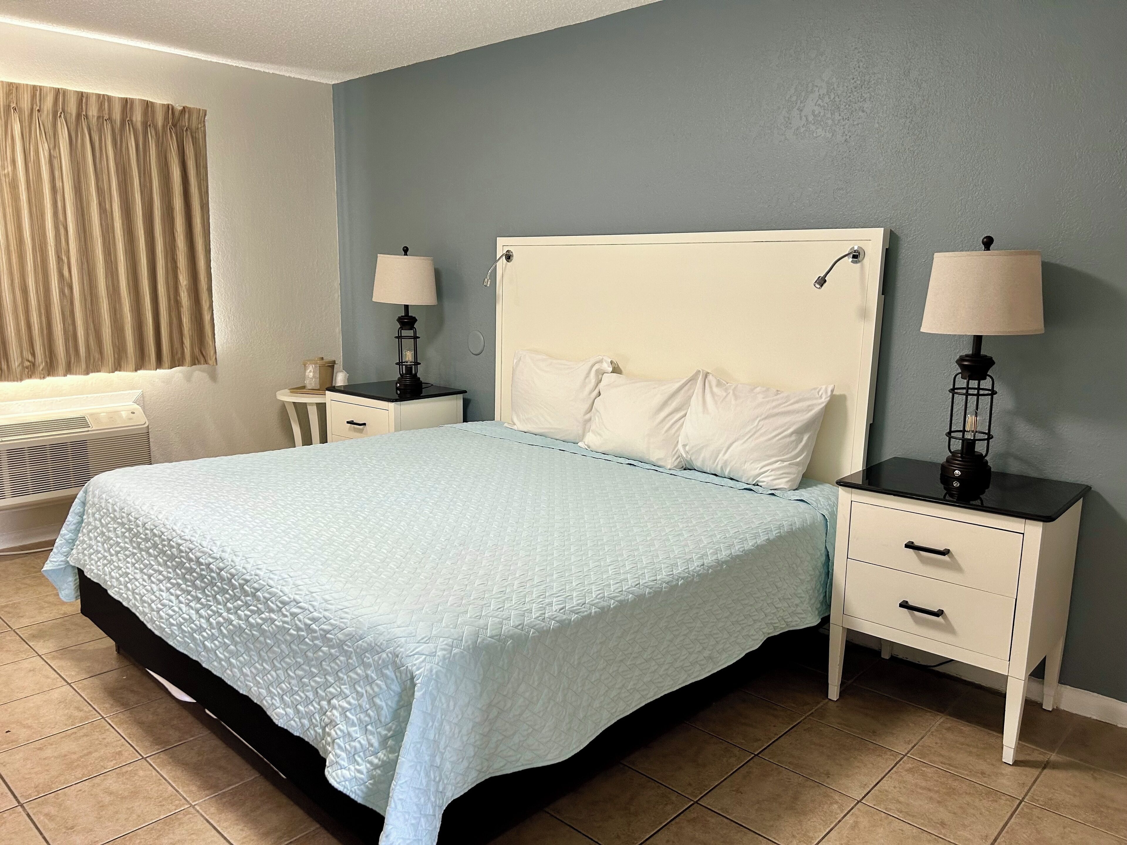 Un dormitorio ordenado con cama, dos mesitas de noche y una ventana con cortinas.