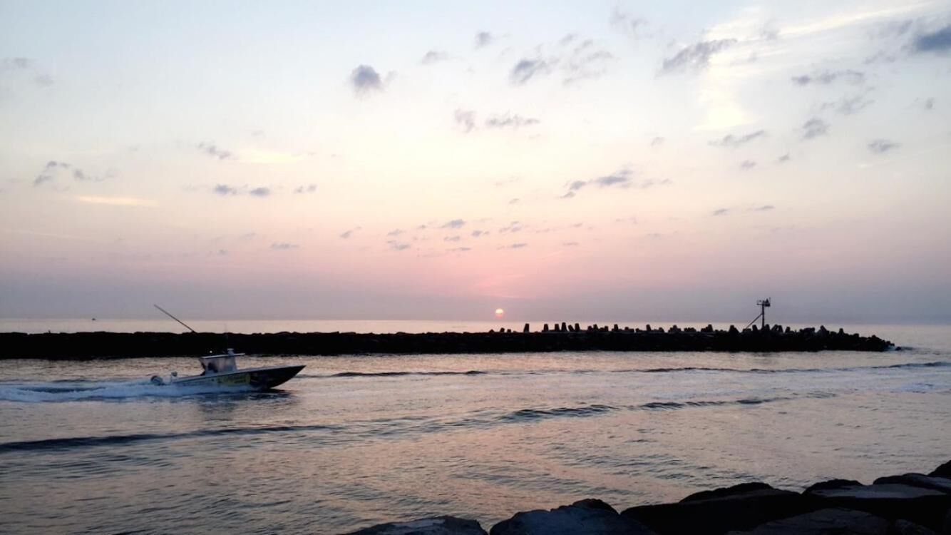 Un barco en aguas tranquilas con un atardecer al fondo y una costa rocosa.