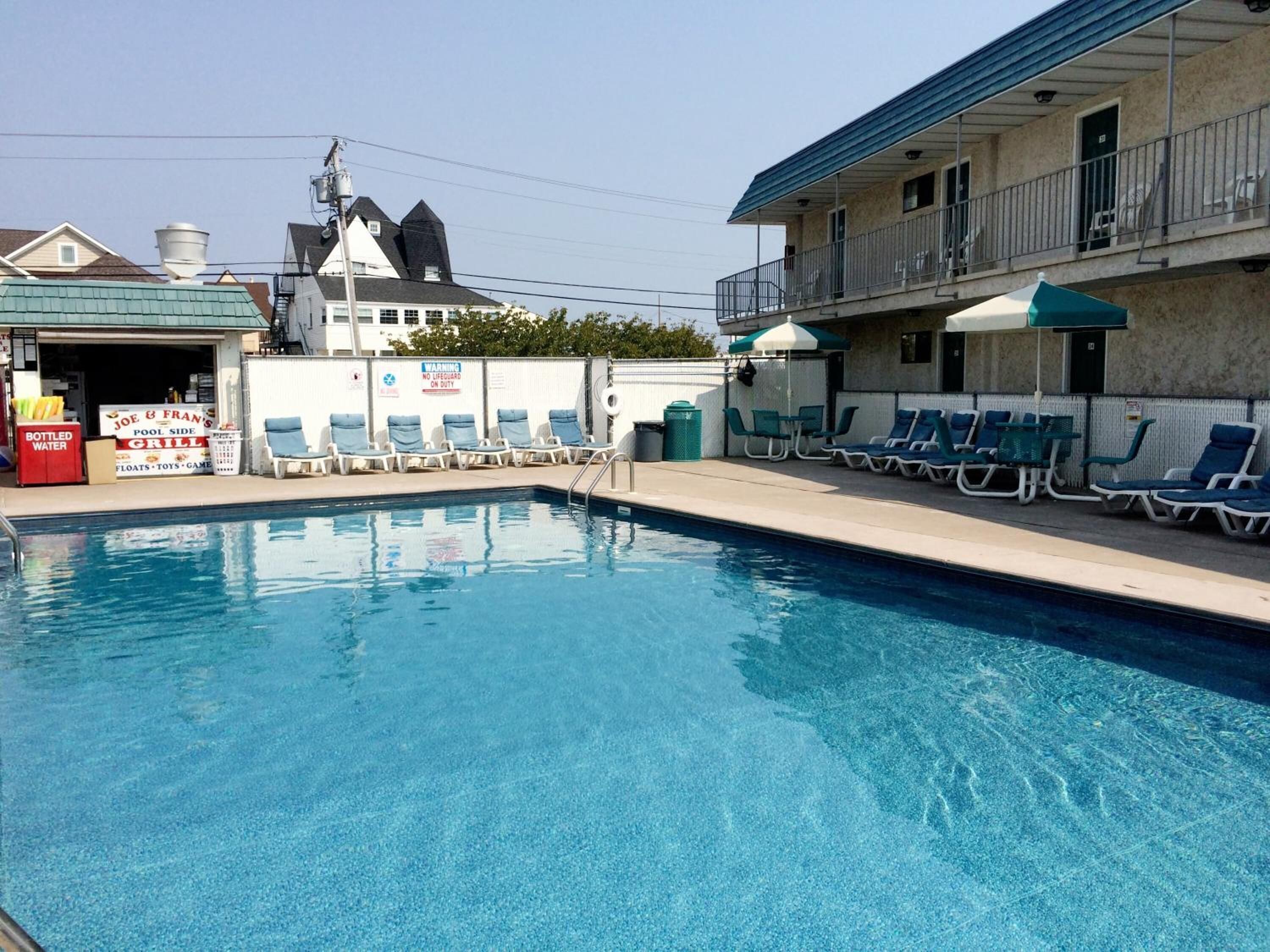 Una piscina con sillas de descanso y un pequeño edificio con un letrero que dice Joe & Fran's Pool Side Grill.