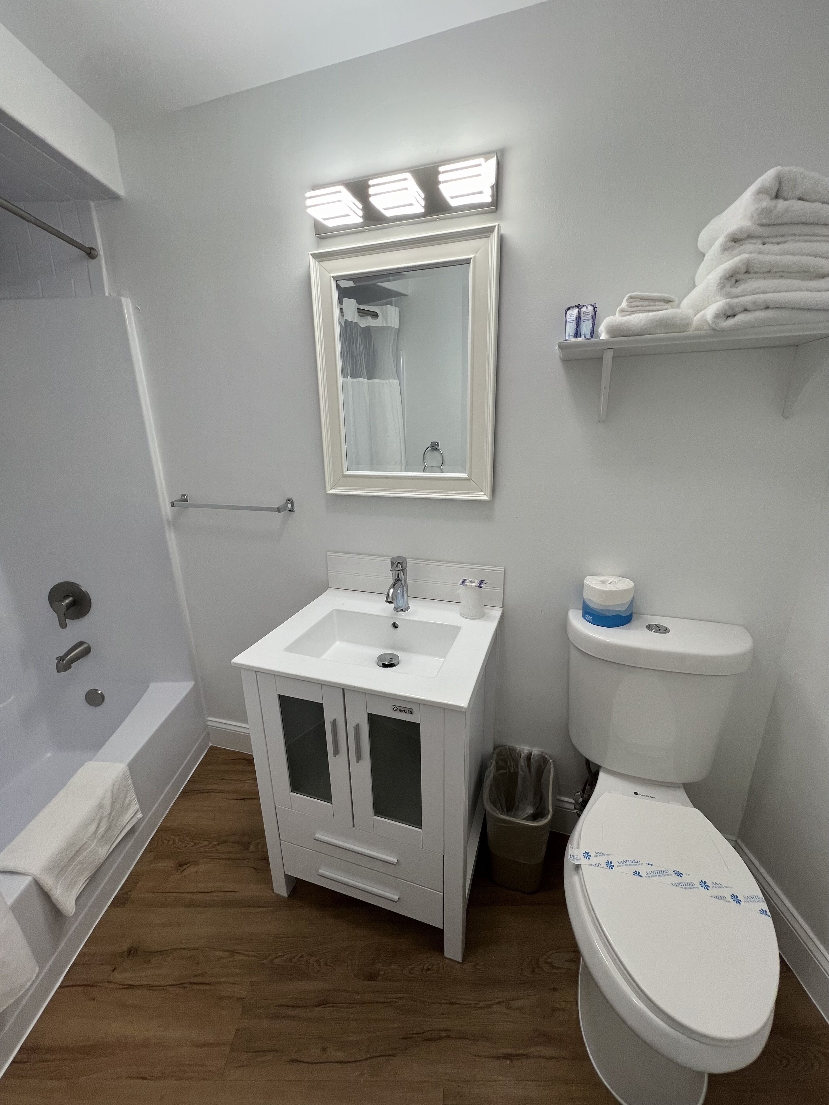 A bathroom with a white sink, mirror, and toilet. There is a towel rack above the sink and a trash can next to the toilet.