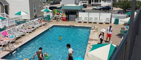 A swimming pool with lounge chairs and umbrellas, surrounded by houses and a small business.