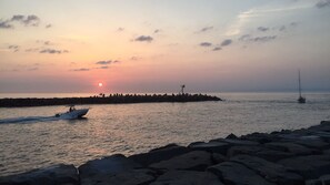 A sunset over a calm sea with a rocky shoreline and a small boat.