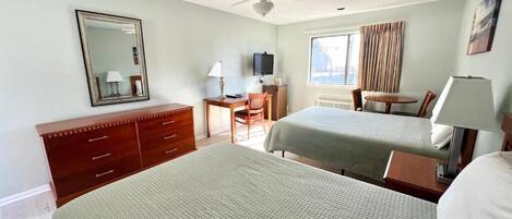 A hotel room with two beds, a desk, a chair, a TV, and a ceiling fan.