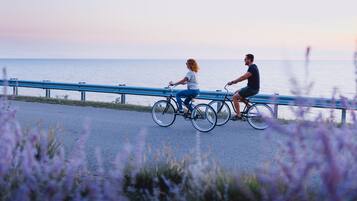 Two people riding bicycles on a paved path beside a body of water.
