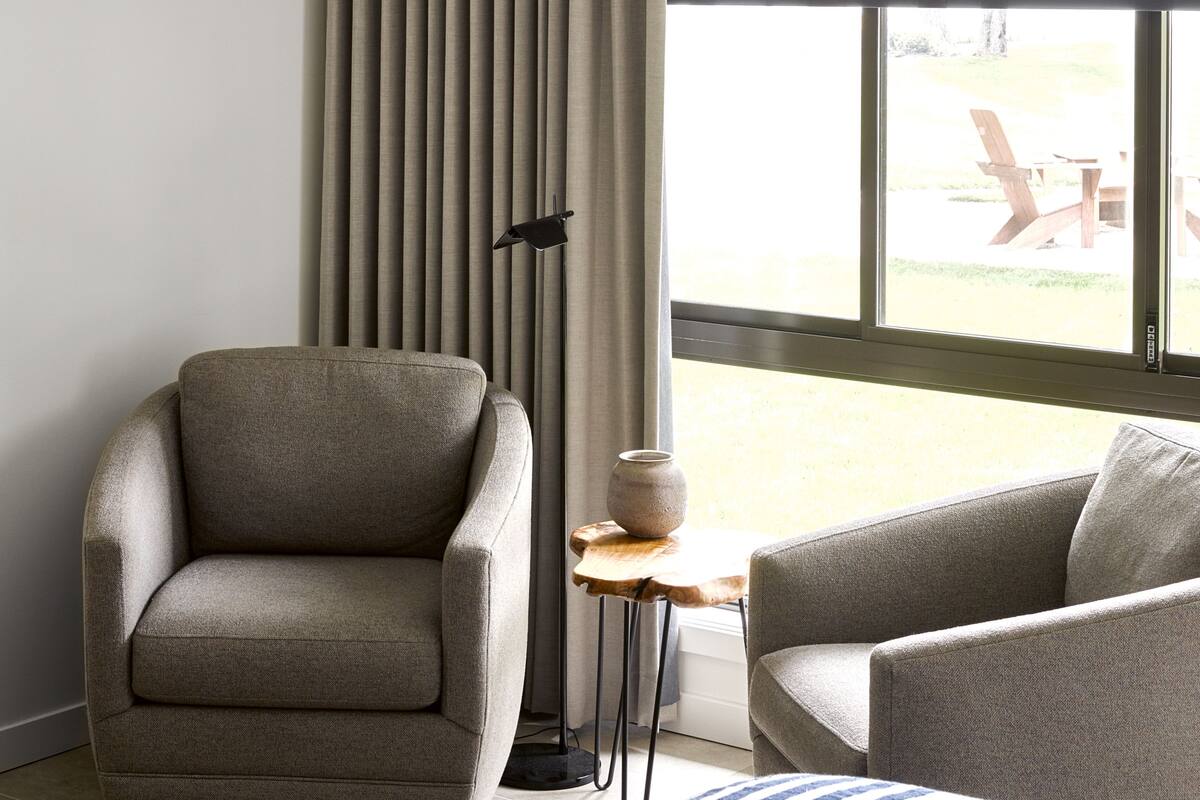 A modern room with a large window, a sofa, a chair, and a small table with a vase.