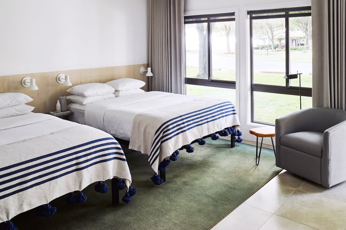 A hotel room with two beds, a chair, and large windows offering a view of the outdoors.