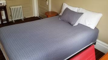 Uma cama bem arrumada com um edredom cinza, um travesseiro branco e um travesseiro cinza acolchoado.