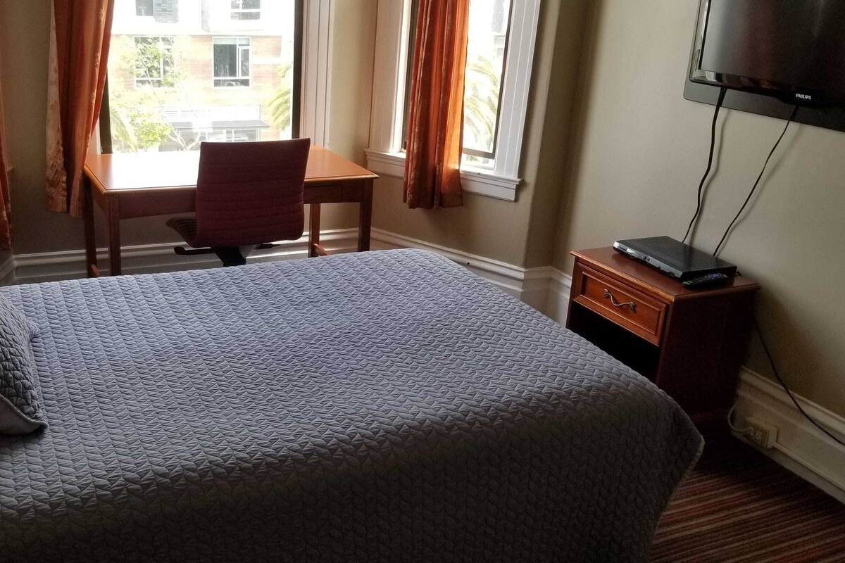 A hotel room with a bed, a desk, a chair, a television, and a window with curtains.