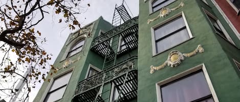 Um edifício de vários andares com fachada verde, molduras de janelas elaboradas e escada de incêndio.