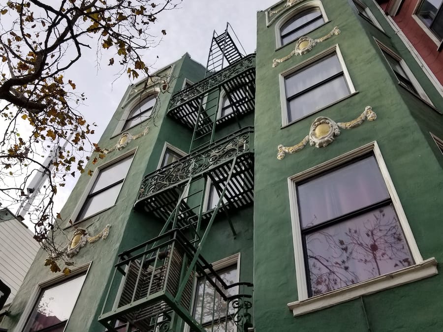 A multi-story building with green facades, ornate window frames, and a fire escape.
