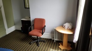 A hotel room with a red office chair, a small wooden table with towels and toiletries, a radiator, and a patterned carpet. - Perramont Hotel (San Francisco)