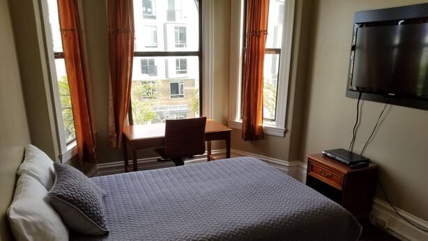 A hotel room with a bed, a desk, a chair, a TV, and a window with curtains. - Perramont Hotel (San Francisco)