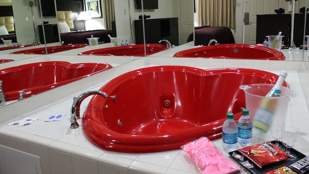 A hotel bathroom with multiple red bathtubs, a large mirror, and various toiletries on the counter.