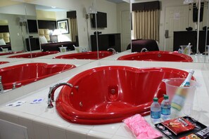 A hotel bathroom with multiple red bathtubs, a large mirror, and various toiletries on the counter. - Apple Inn (Dallas)