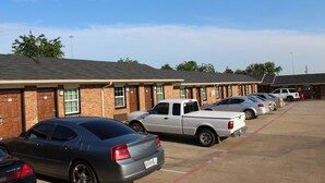 A parking lot with several cars and a building with brick walls and multiple windows.