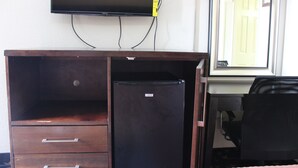 A room with a TV mounted on the wall, a desk with a chair, and a refrigerator.