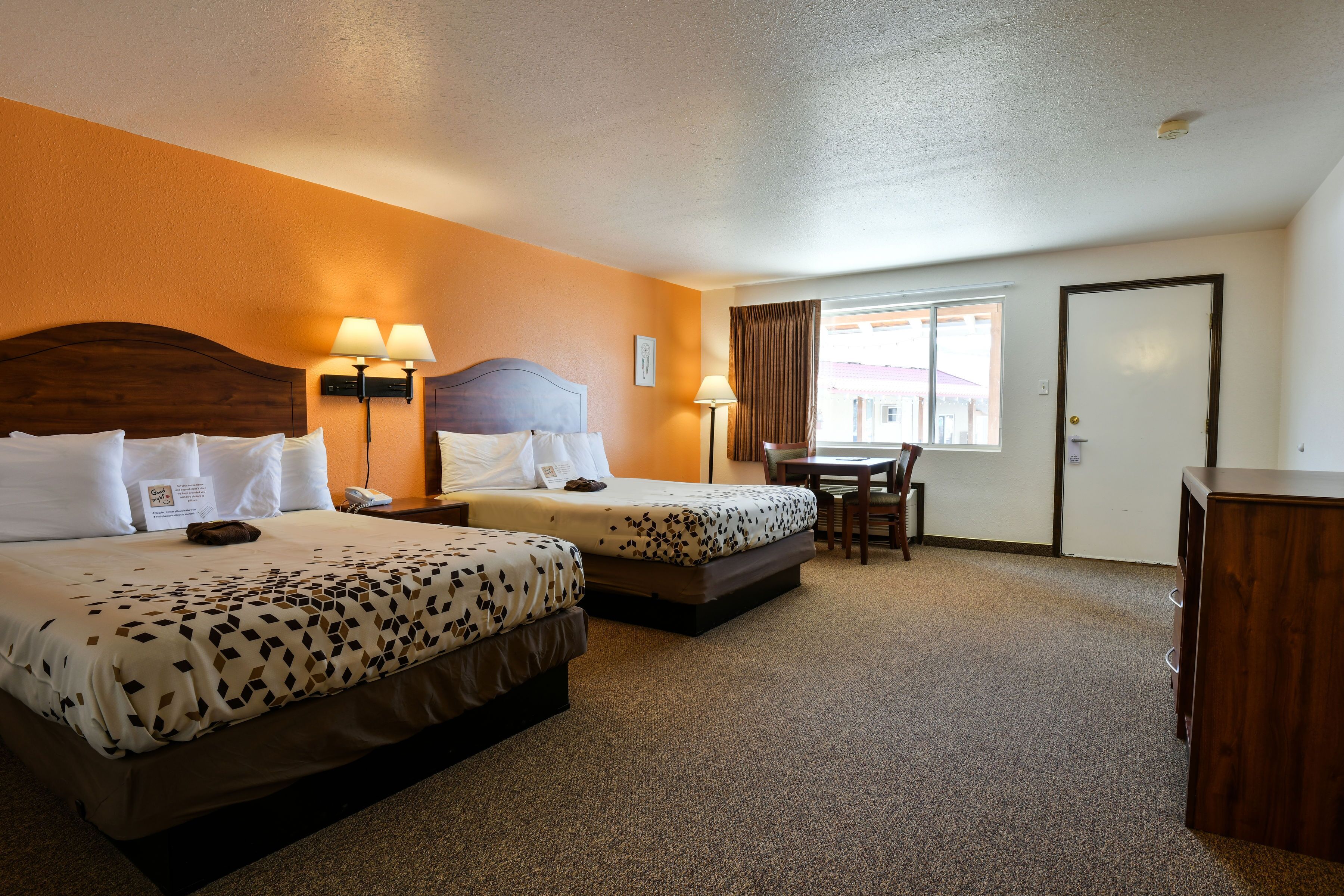 Quarto de hotel com duas camas, uma escrivaninha e uma cadeira.