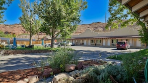 A motel with a parking lot, a covered outdoor seating area, and a mountain backdrop. - Adventure Inn & Motel (Moab)