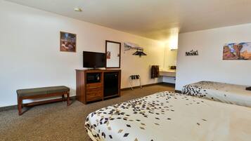 A hotel room with two beds, a bench, a TV, a desk, and a mirror.