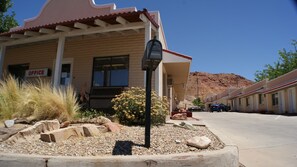 A building with an 'OFFICE' sign, a mailbox, and a parking lot with a mountain in the background.