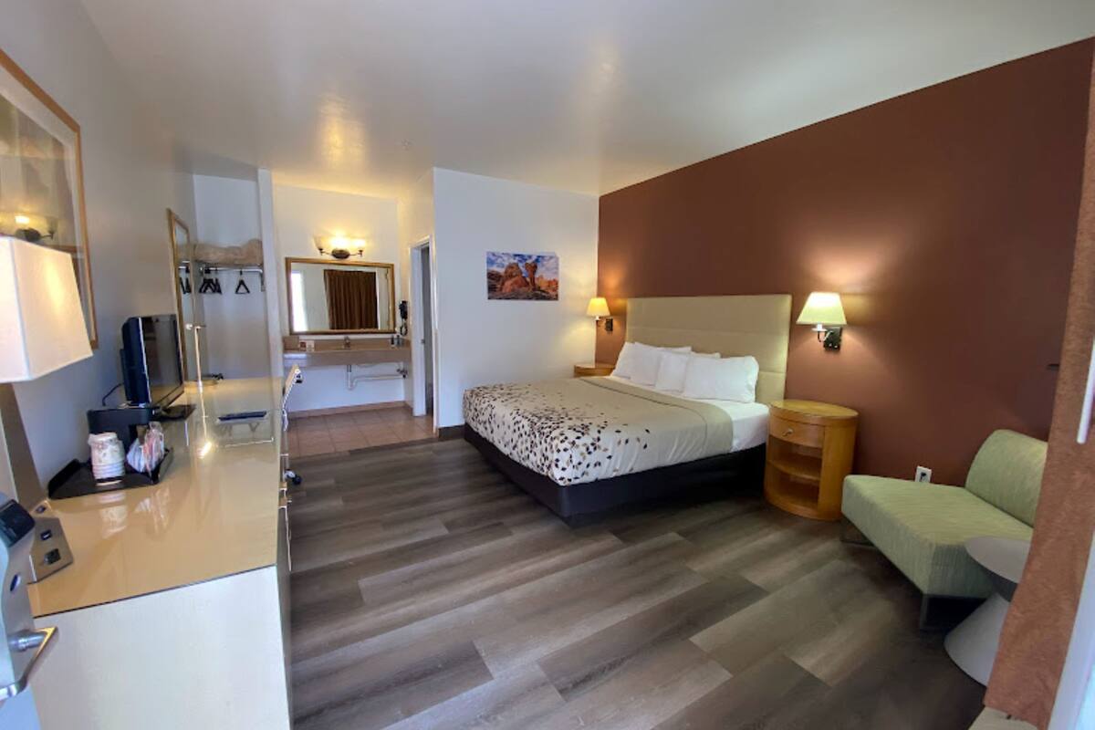 A hotel room with a bed, bedside table, lamp, and a small seating area.