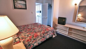Un dormitorio con cama, televisor, lámpara, c ómoda y armario.
