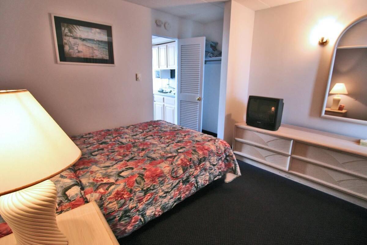 A bedroom with a bed, a TV, a lamp, a dresser, and a closet.