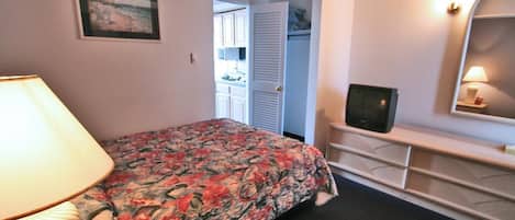 Un dormitorio con cama, televisor, lámpara, cómoda y armario.