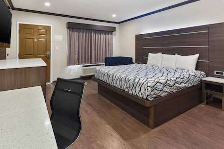 A hotel room with a large bed, a desk, a chair, a wardrobe, and a window with curtains.
