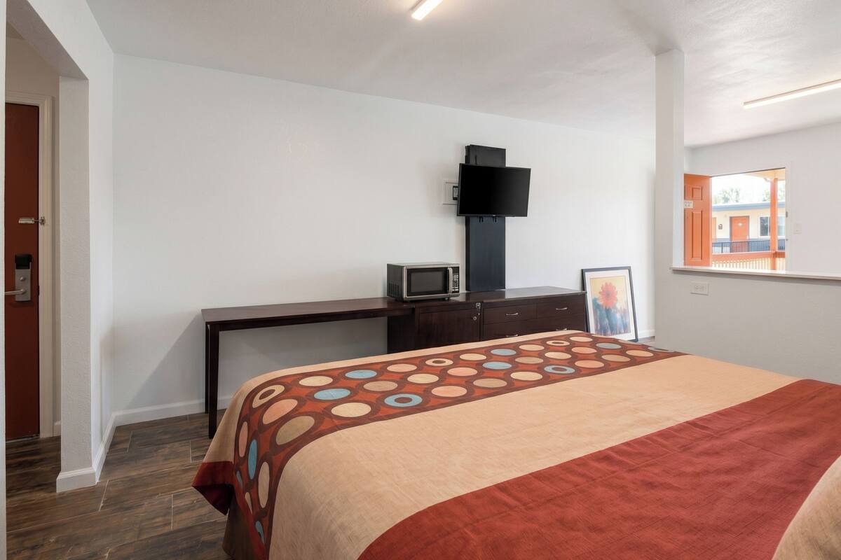 A bedroom with a bed, a desk, a television, and a window.