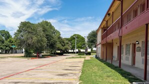 Un hôtel doté d’un parking, un bâtiment à la façade rouge et un arbre au premier plan.