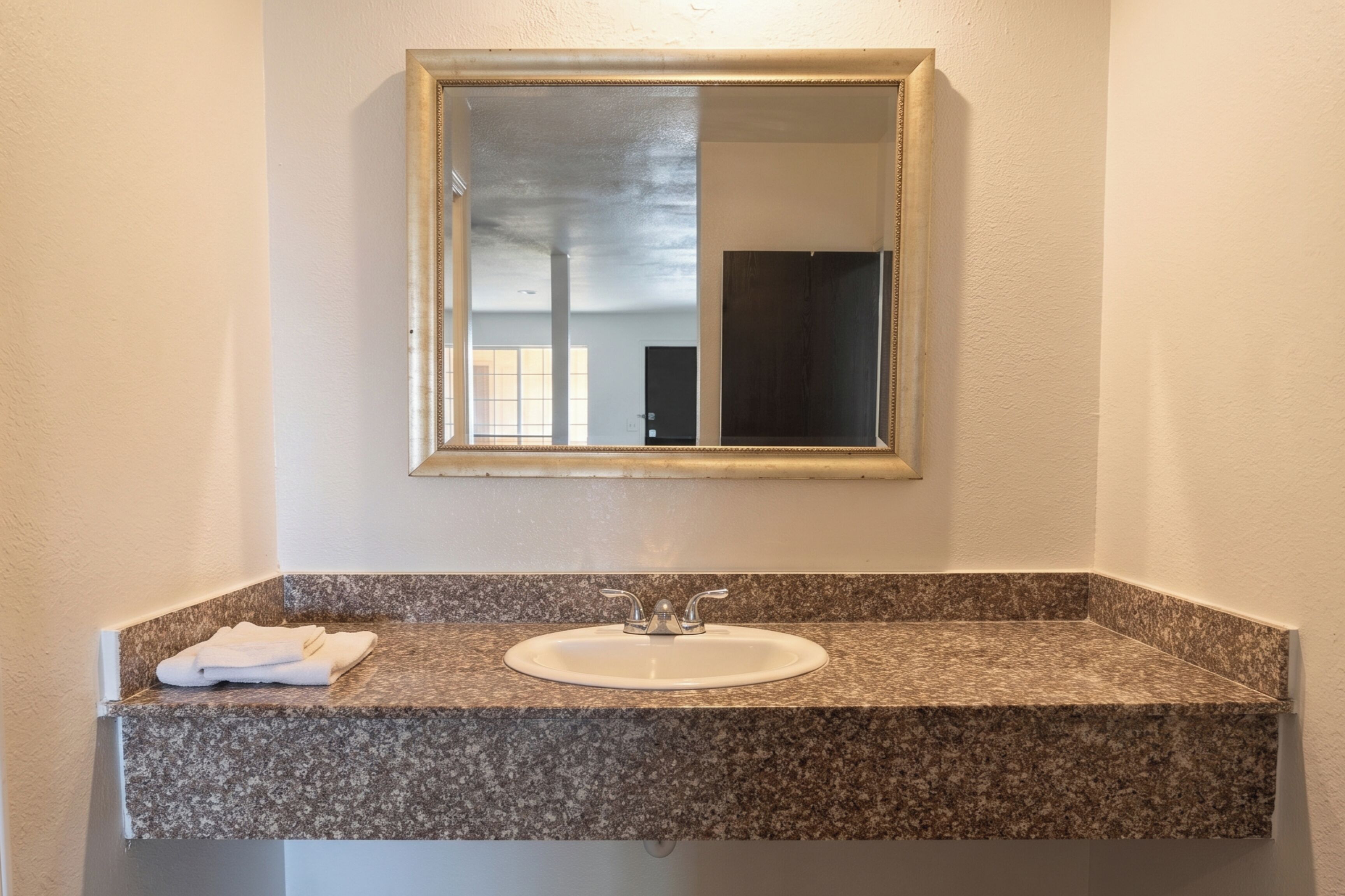 Un baño con encimera de granito, un lavabo blanco y un espejo con marco dorado.