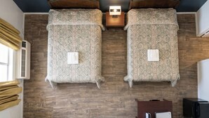 Une chambre avec deux lits, un plancher en bois, un luminaire fixé au mur et une petite table en bois.