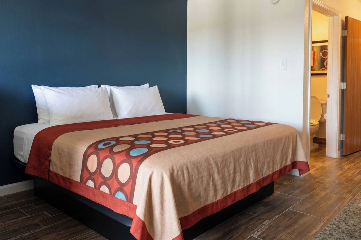A bed with a patterned bedspread, a dark blue wall, and a wooden floor.