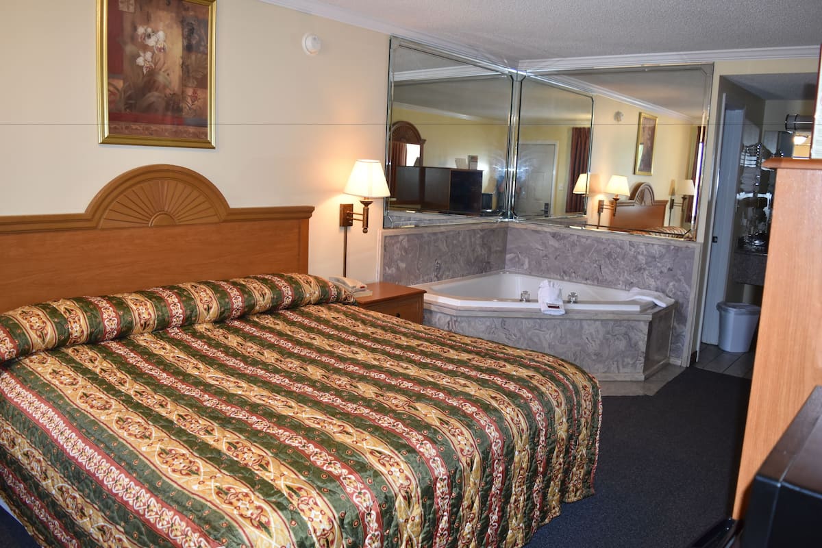 A hotel room with a bed, a large mirror, a bathroom with a bathtub, and a wooden headboard.