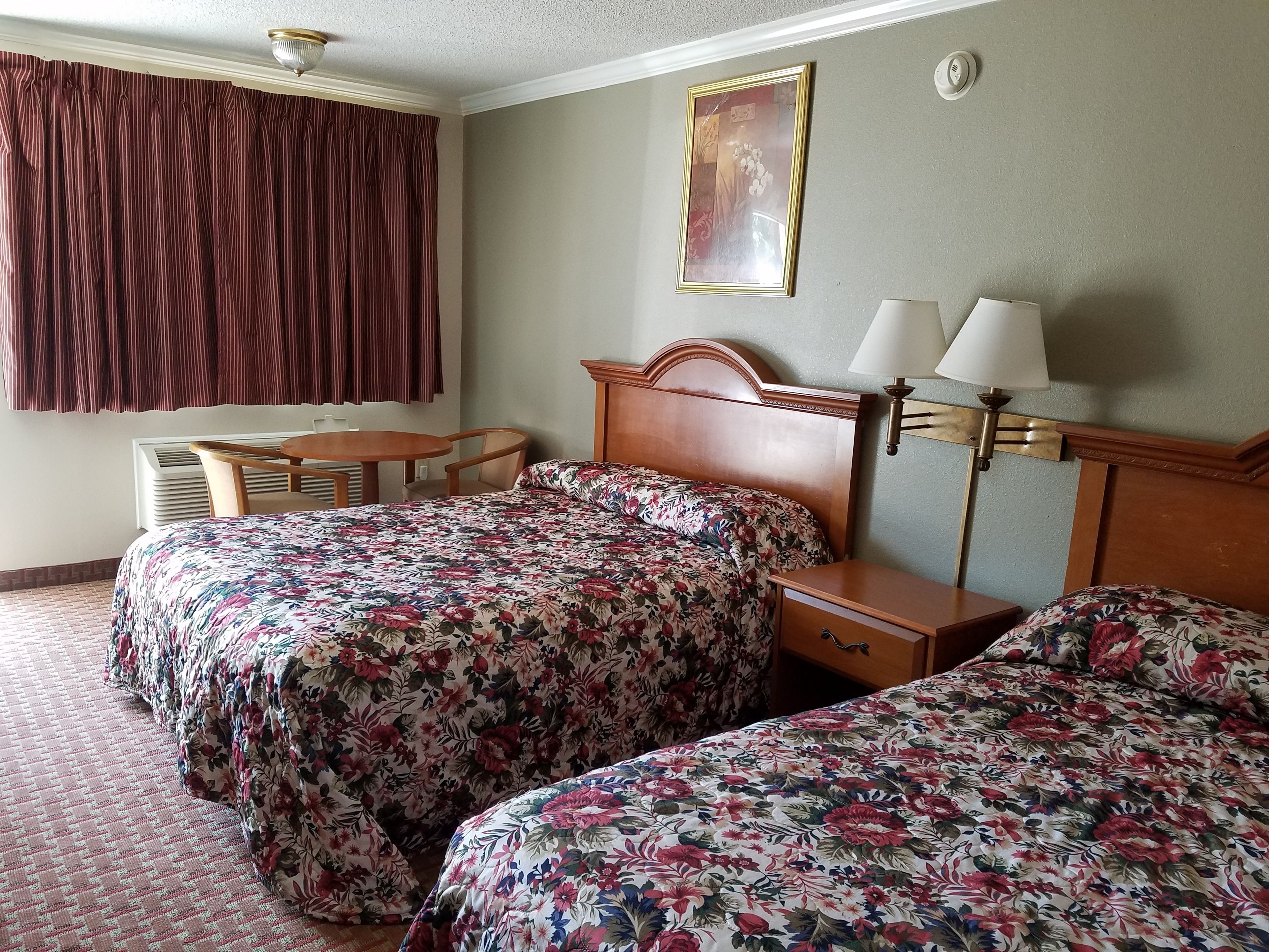Une chambre d’hôtel avec deux lits, une tête de lit en bois, une petite table, une chaise, une lampe et un tableau au mur.