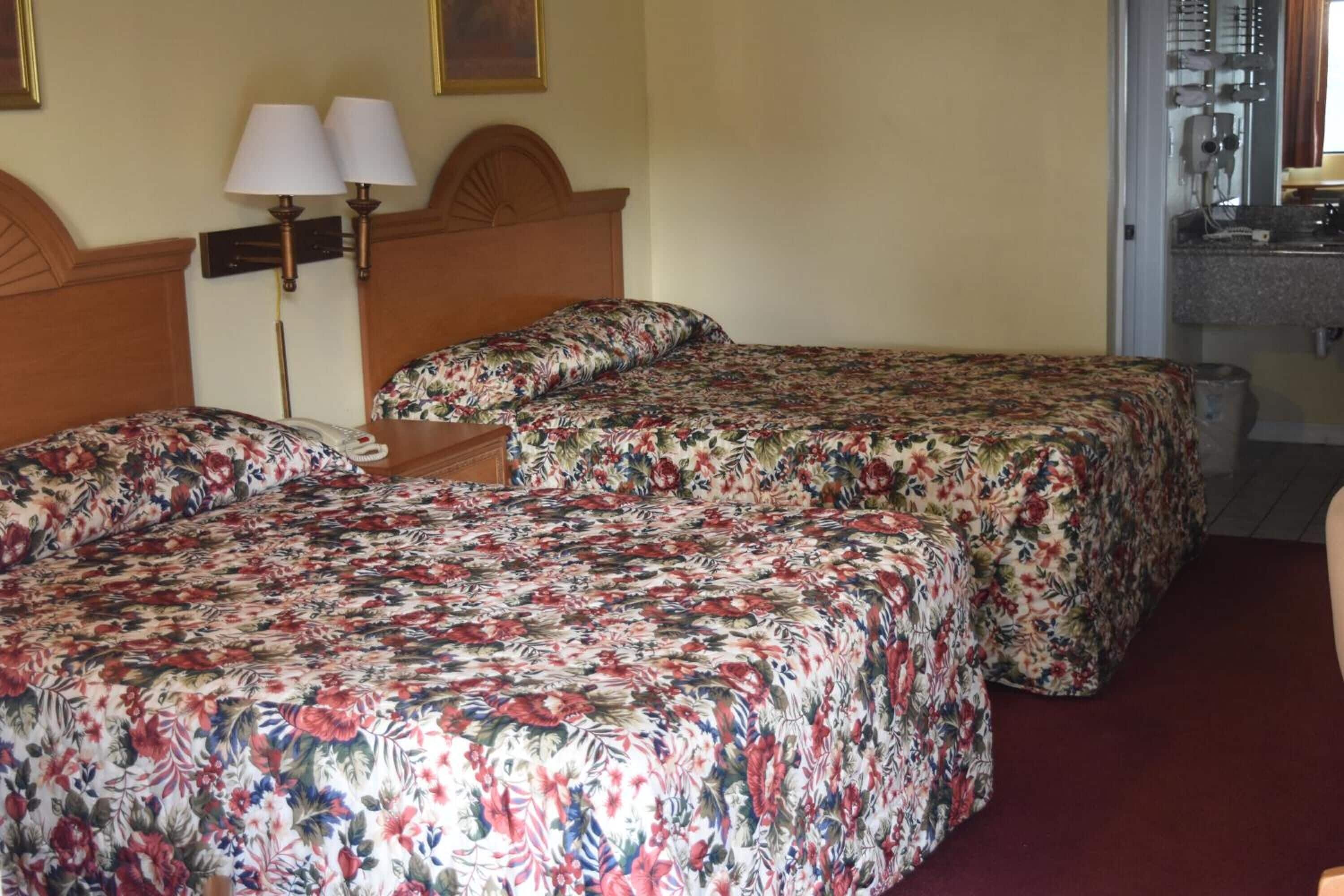 Een hotelkamer met twee bedden, elk voorzien van bloemenbeddengoed, een houten hoofdeinde en een nachtkastje met lampen.