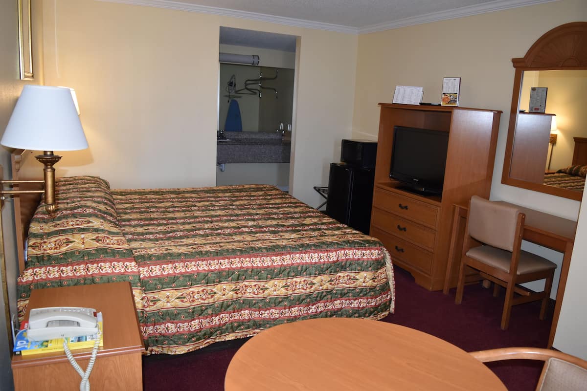 A hotel room with a bed, a desk with a chair, a television, and a telephone.