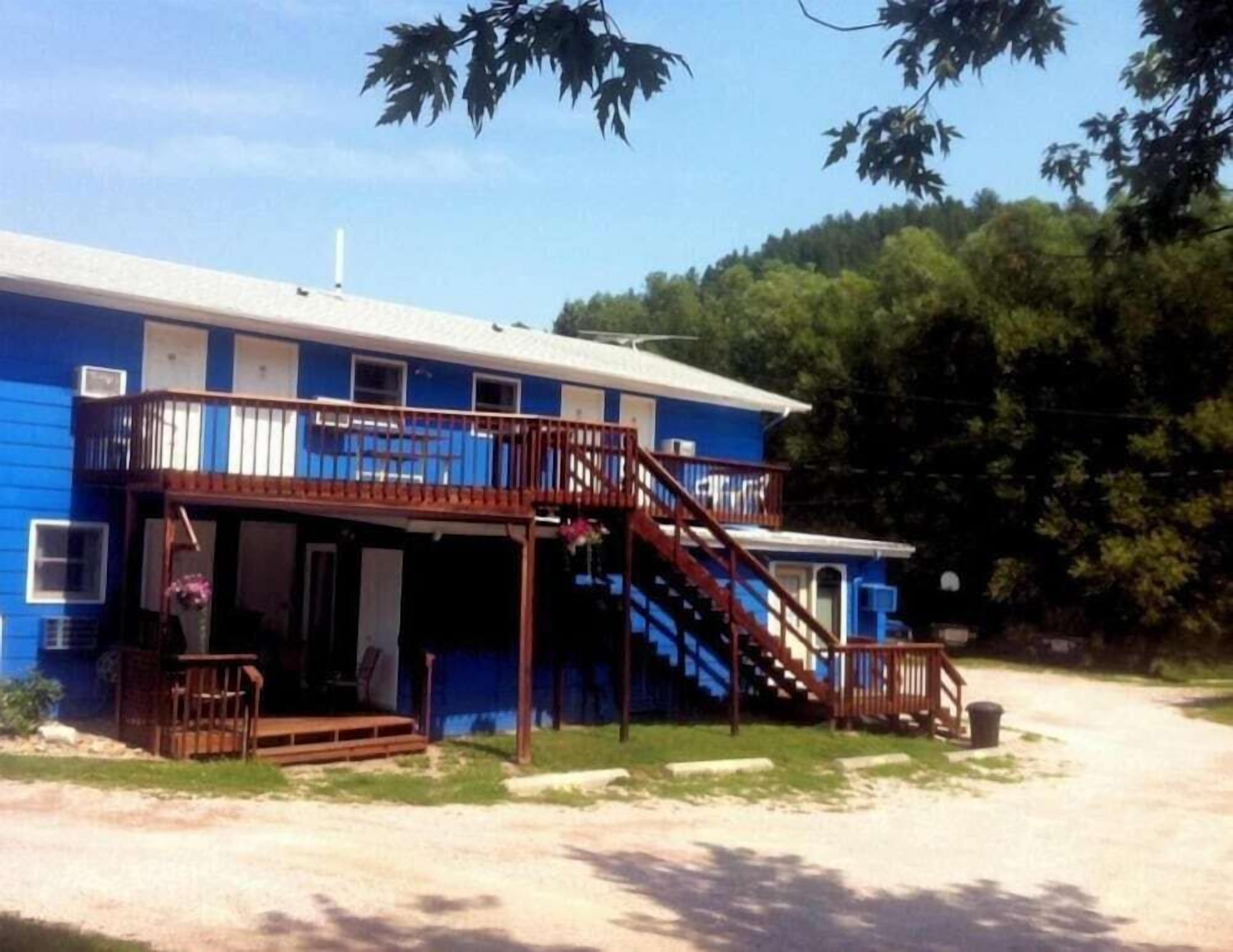 A blue building with a wooden staircase leading to a balcony, a front porch, and a small attached structure.