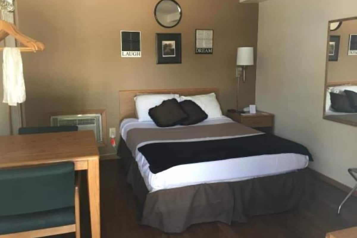 Habitación de hotel con cama, escritorio, silla, mesita de noche, lámpara y espejo.