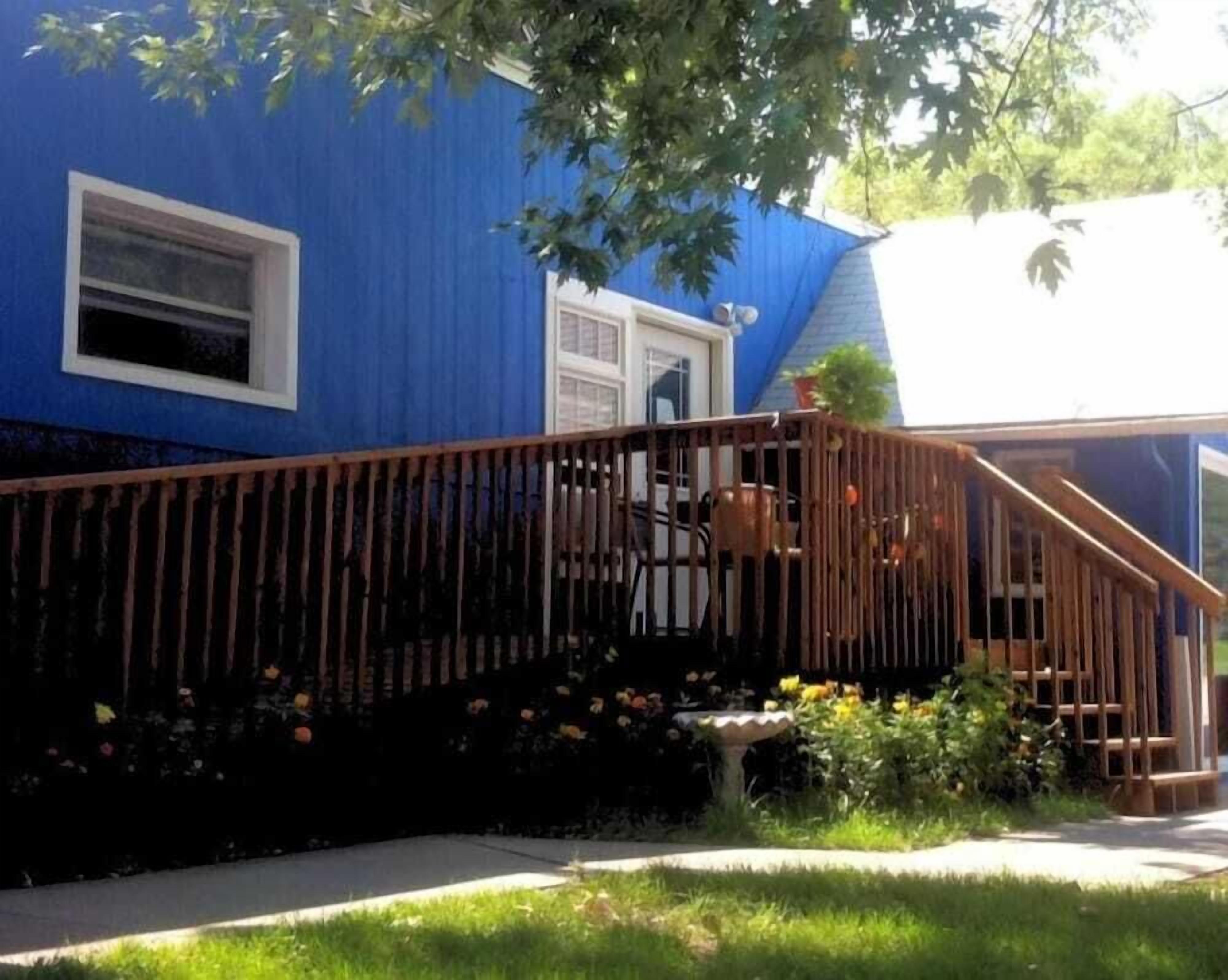 Une maison bleue avec une terrasse en bois et un petit jardin.